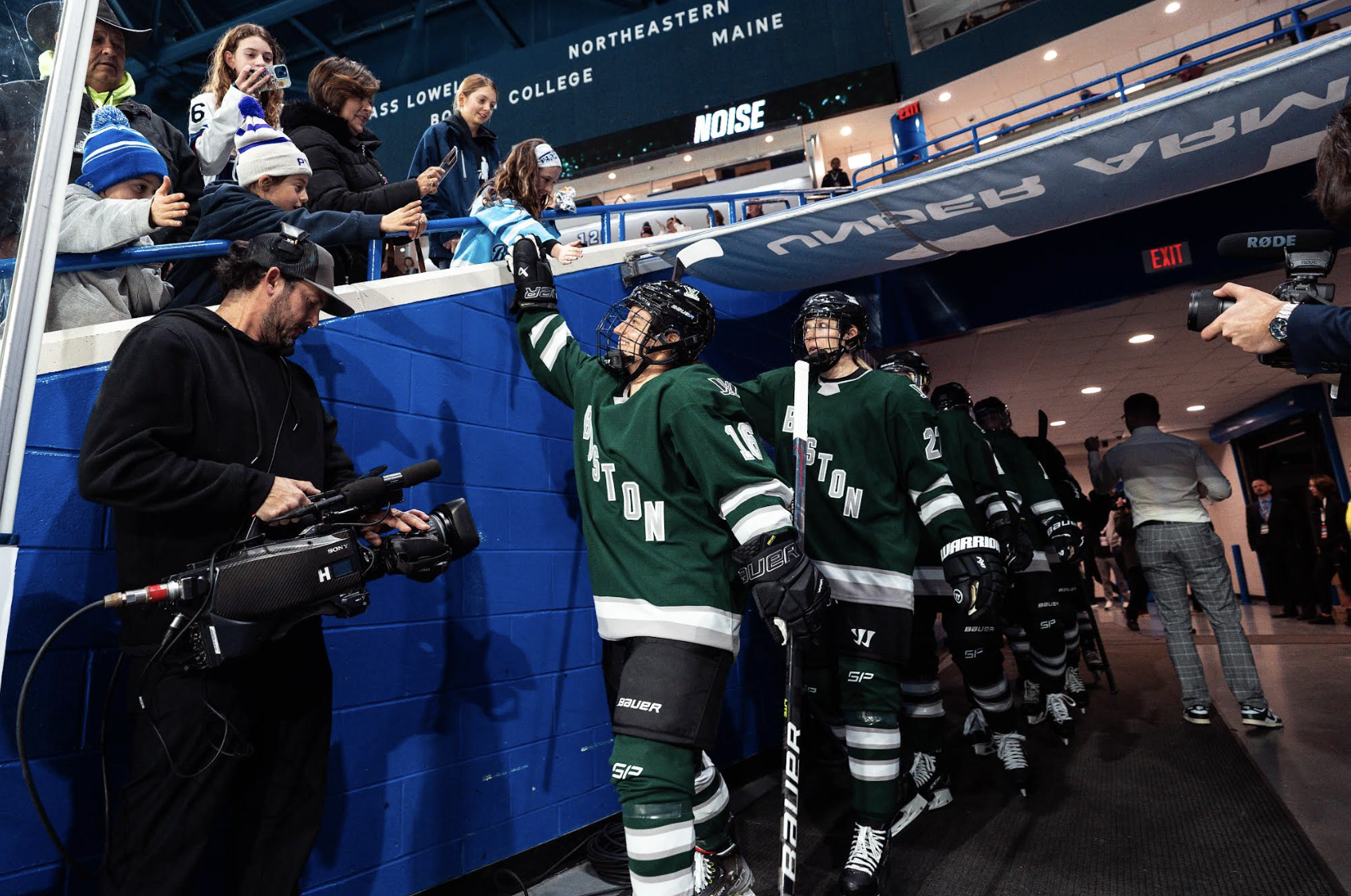 Members of PWHL Boston, wearing green jerseys, exit the locker room tunnel and high-fans prior to a game against PWHL Minnesota.